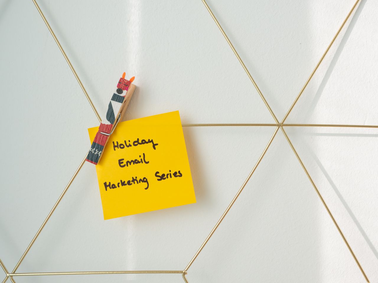 Post-it jaune vif accroché à un mur maquette par une pince, avec un message de marketing par e-mail pour les fêtes.